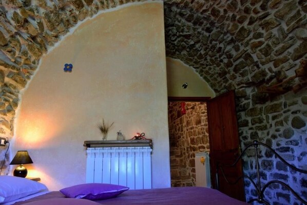 A bedroom with a stone wall, a radiator, and a bed with purple bedding.
