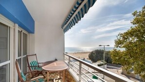 Un balcón con mesa y sillas, vista a la playa y un estacionamiento.