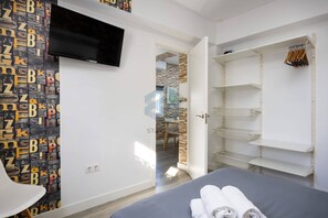 A bedroom with a bed, a TV mounted on the wall, and a wardrobe with hanging space.