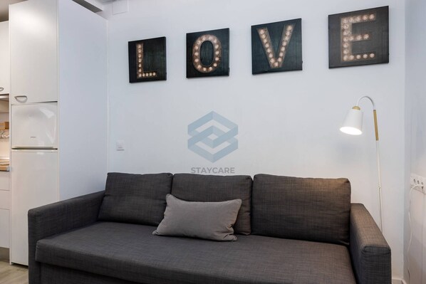 A modern interior with a grey sofa, a wall-mounted light fixture, and illuminated letters spelling 'LOVE'.
