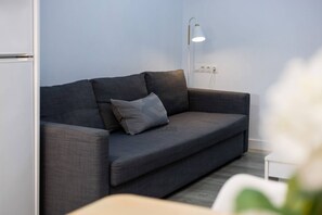 A modern living room with a dark grey sofa, a single grey pillow, a white side table, and a floor lamp.