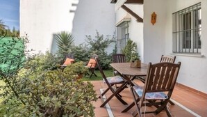 An outdoor patio with a wooden table and chairs, surrounded by potted plants and a white wall. - El Paraíso del Golf free parking by Staycare (Rota)
