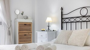 A neatly made bed with rolled towels, a bedside table with a lamp, a wooden dresser, and a metal headboard. - El Paraíso del Golf free parking by Staycare (Rota)