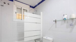 A bathroom with a glass-enclosed shower, a toilet, and a shelf with toiletries.