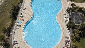 An aerial view of a large, kidney-shaped swimming pool surrounded by a deck with lounge chairs and umbrellas.
