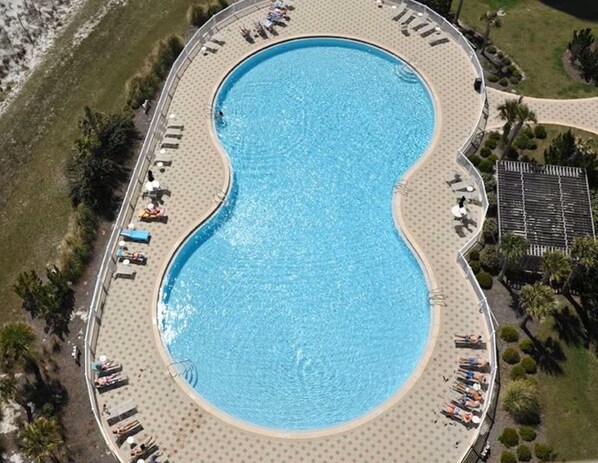 An aerial view of a large, kidney-shaped swimming pool surrounded by a deck with lounge chairs and umbrellas. - Beach Colony West 11E / Gulf Front w/Beach Service & Onsite Management (Navarre Beach)