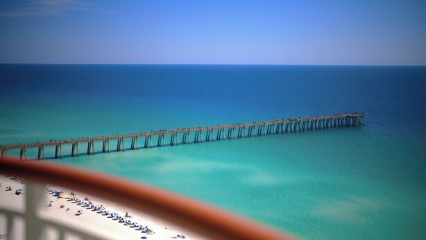 A pier extending into a clear blue sea with a beach in the foreground.