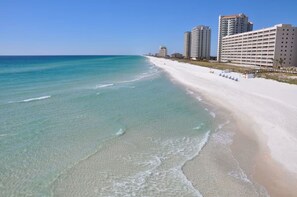 A beach with clear turquoise water, a sandy shore, and high-rise buildings in the background.