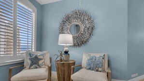 A room with two upholstered chairs, a round mirror, a lamp, and a wicker side table.