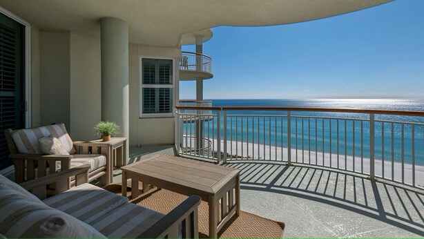 A balcony with a view of the ocean, a wooden table, and a striped sofa. - Beach Colony West 11E / Gulf Front w/Beach Service & Onsite Management (Navarre Beach)
