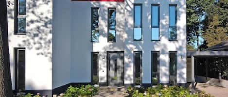 A modern two-story building with a flat roof, large windows, and a well-maintained lawn.