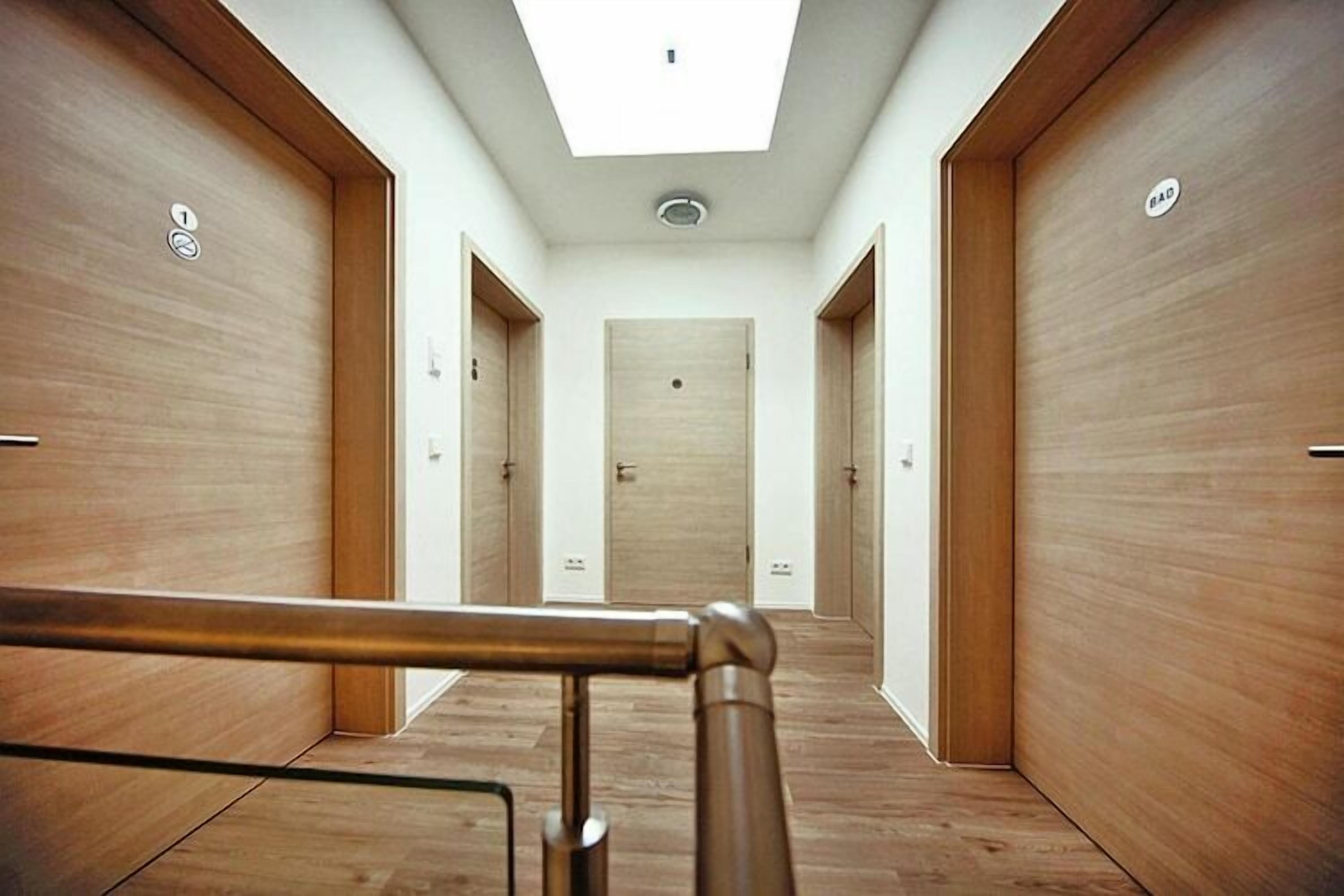 A hallway with wooden doors, a skylight, and a metal handrail.