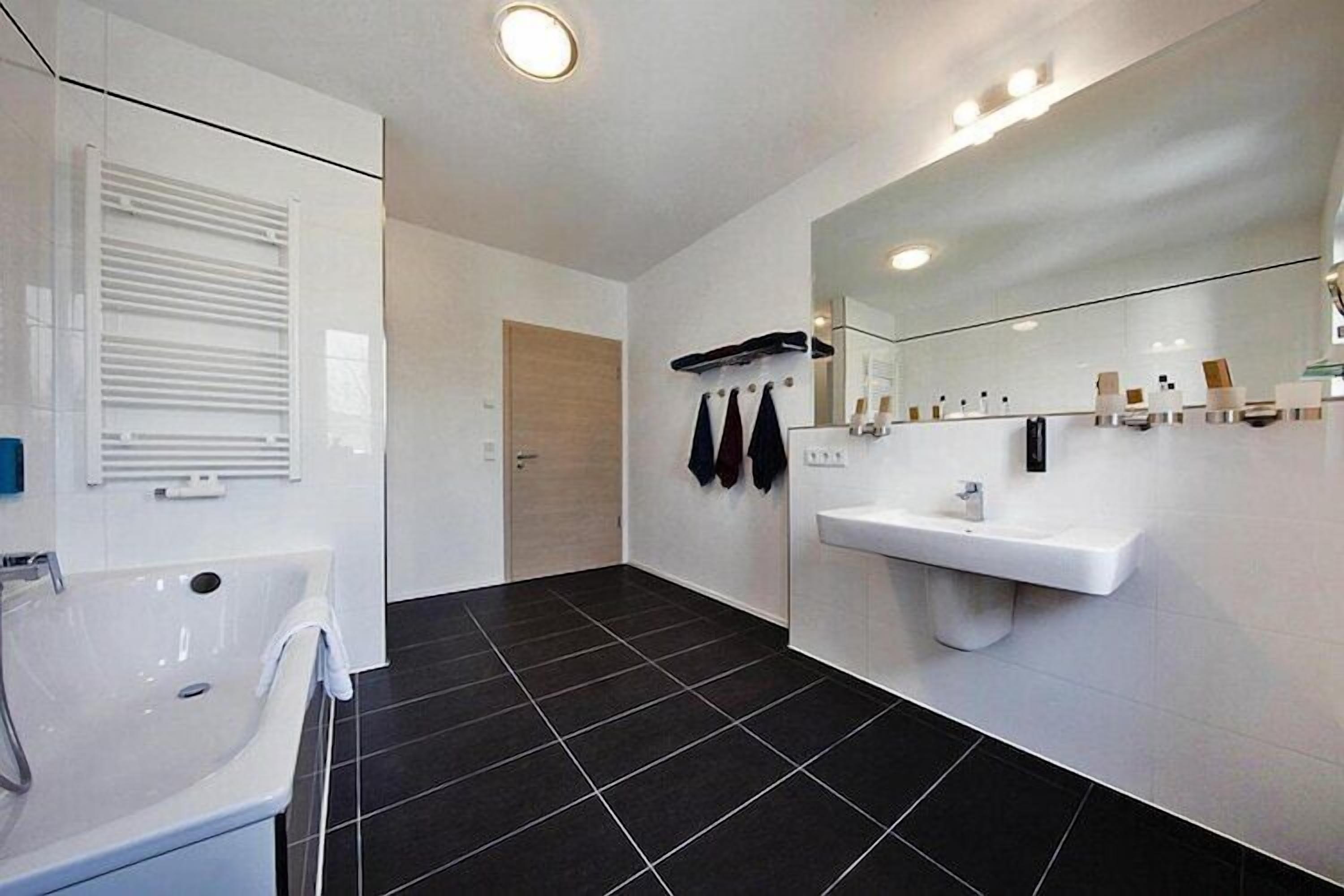 A modern bathroom with a white sink, mirror, and black-tiled floor.