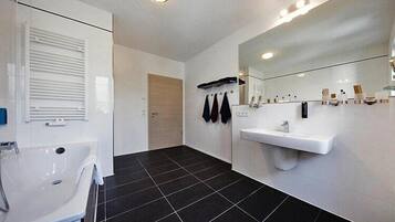 A modern bathroom with a white sink, mirror, and black-tiled floor.