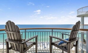 Un balcón con dos sillas Adirondack mirando una playa de aguas turquesas cristalinas y un edificio blanco al fondo.