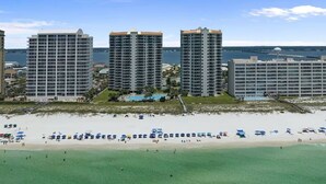 Un hôtel en bord de mer composé de plusieurs immeubles de grande hauteur, une plage de sable avec des parasols et une vue sur l’océan.