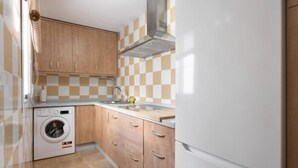 A compact kitchen with wooden cabinets, a built-in washing machine, and a white refrigerator. - Isaac Peral by Staycare (Rota)