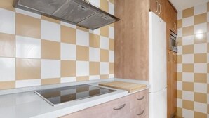 A kitchen with a checkered tile backsplash, a stainless steel range hood, a built-in oven, and a white refrigerator. - Isaac Peral by Staycare (Rota)