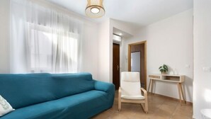 A living room with a teal sofa, a white armchair, a wooden desk, and a small plant. - Isaac Peral by Staycare (Rota)