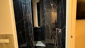 Une salle de bain moderne avec des murs en marbre noir, un espace douche et un meuble-lavabo.