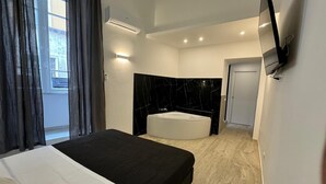 Une chambre d’hôtel moderne dotée d’un grand lit, d’une salle de bain séparée avec baignoire et d’un téléviseur à écran plat fixé au mur.