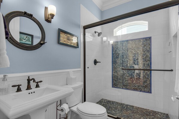 A bathroom with a white sink, a toilet, a shower with a glass door, and a mirror with a round frame.