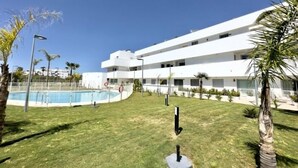 A modern multi-story building with a swimming pool, surrounded by palm trees and a well-maintained lawn.