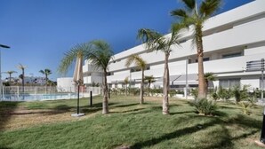 A courtyard with palm trees, a pool, and a white building with multiple floors.