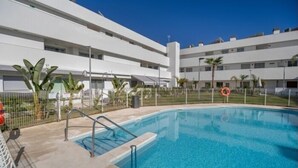 A modern hotel with a swimming pool, multiple floors, and a fenced area with palm trees.