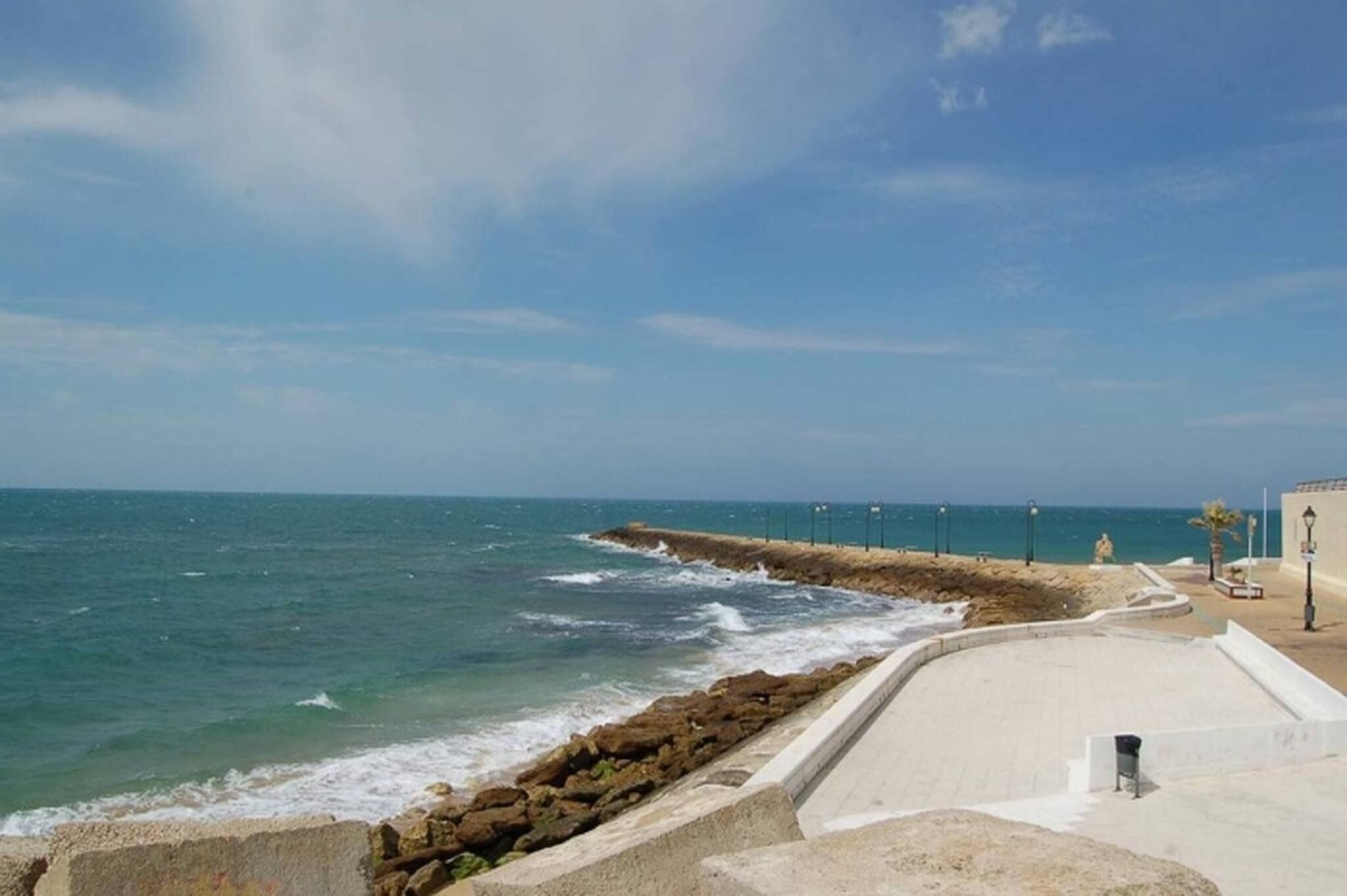 A coastal promenade with a stone sea wall, benches, and street lamps.