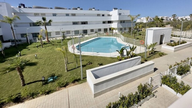 Un bâtiment moderne doté d’une piscine, entouré d’une pelouse bien entretenue et de palmiers.