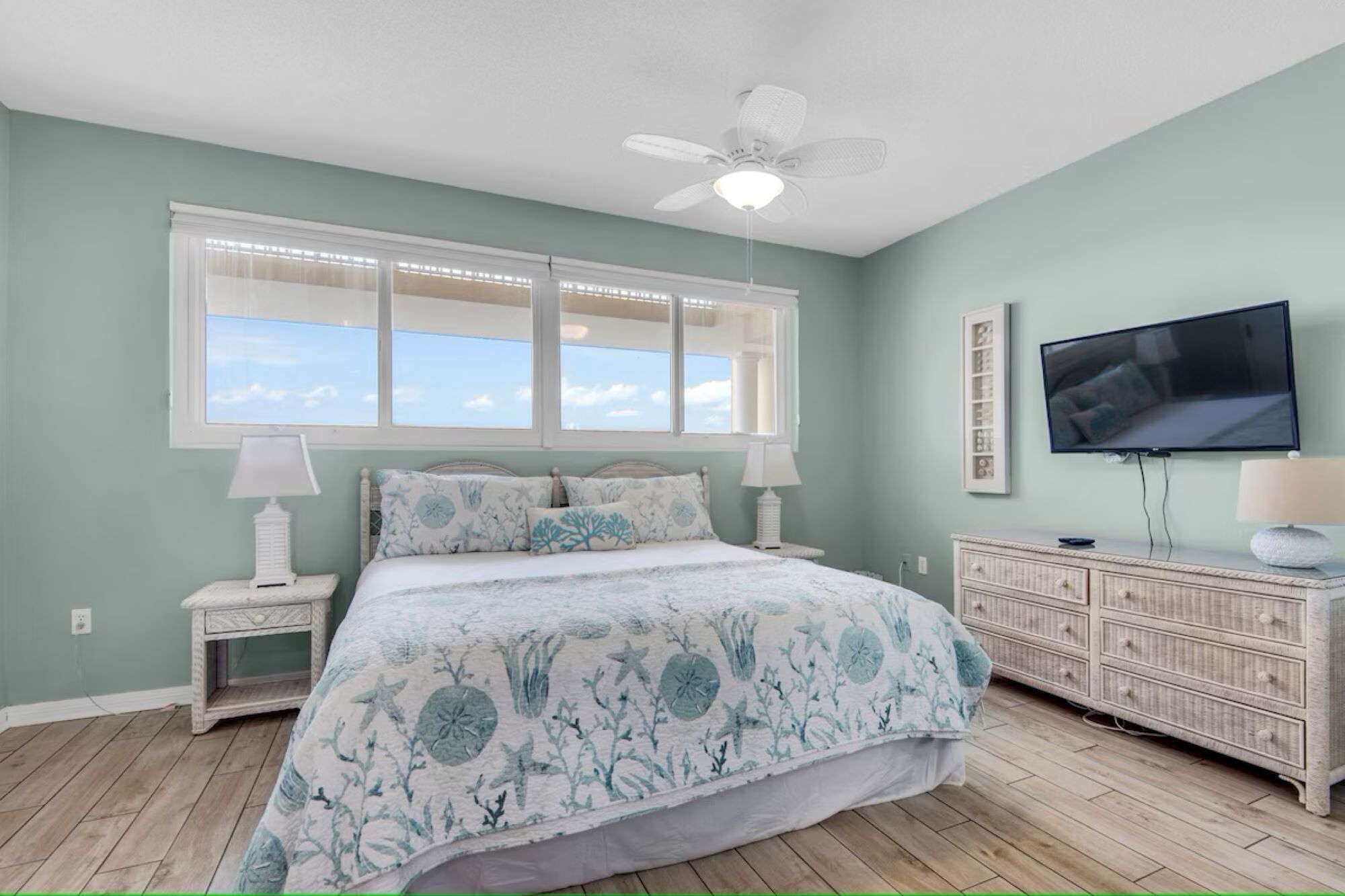 A bedroom with a bed, a ceiling fan, a TV, a dresser, and a window with blinds.