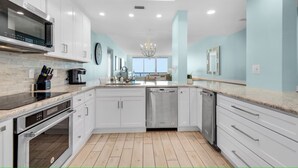 A modern kitchen with white cabinets, stainless steel appliances, and a large window providing natural light. - 12th fl Beachfront 3BR/3BA & Beach Service / Xtra Fridge & Icemaker Sleeps 8 (Navarre Beach)