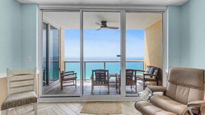 A balcony with a view of the ocean, a ceiling fan, and a leather sofa. - 12th fl Beachfront 3BR/3BA & Beach Service / Xtra Fridge & Icemaker Sleeps 8 (Navarre Beach)