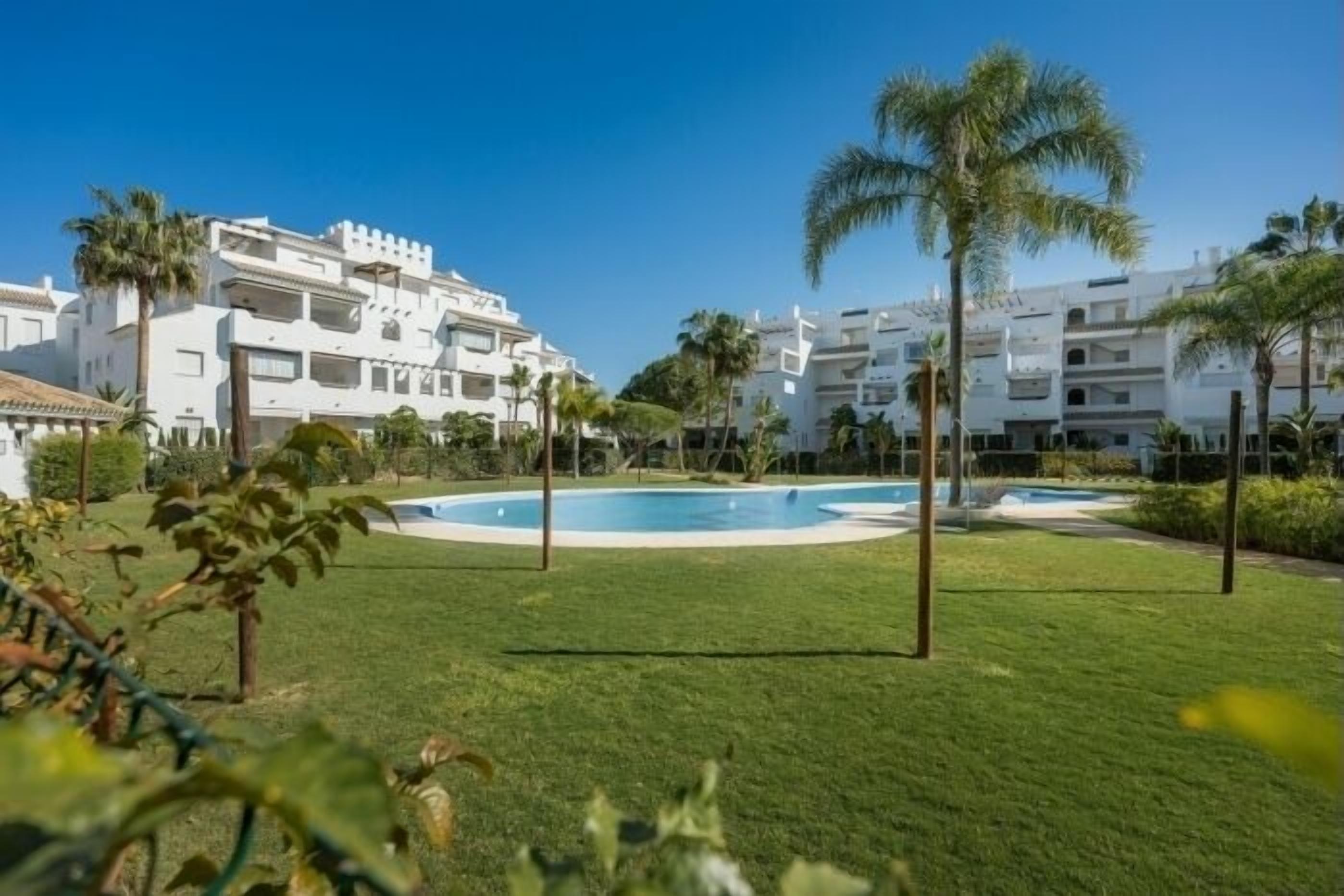 Un complexe hôtelier avec des bâtiments blancs, une piscine et des palmiers.