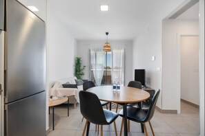 A modern dining area with a round table, chairs, a sofa, and a refrigerator. - Dunas Candor free parking by Staycare (Rota)