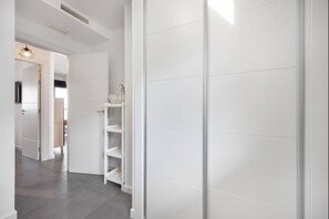 A hallway with a white wardrobe, a white shelf unit, and a hanging light fixture.