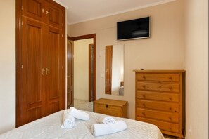 Ein Schlafzimmer mit einem Bett, einer Holzkommode, einem Spiegel und einem Fernseher an der Wand.