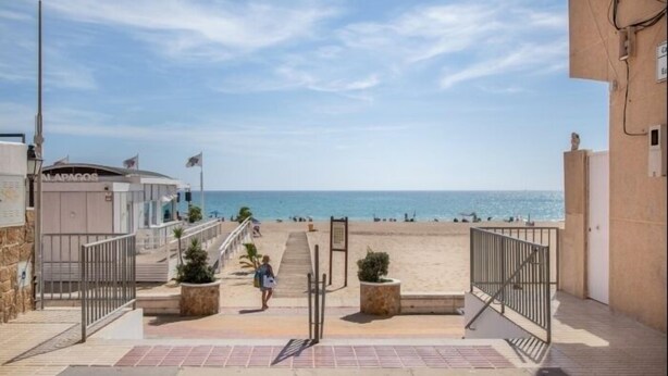 A beachfront property with a staircase leading to a sandy beach, a sign for 'MARIGOS', and a clear view of the sea.