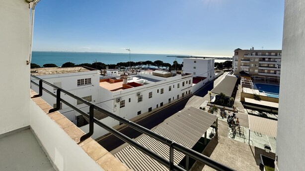 Vista desde un balcón sobre una zona costera con edificios, una piscina y cielo despejado.