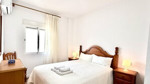 Un dormitorio ordenado con cama de madera, mesitas de noche con lámparas, un escritorio de madera y una ventana con cortinas.