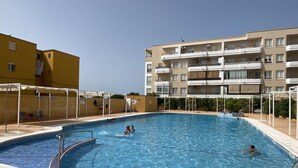 Una piscina con agua azul cristalina, rodeada por una solana con baldosas. Hay sillas de descanso y sombrillas alrededor de la piscina.
