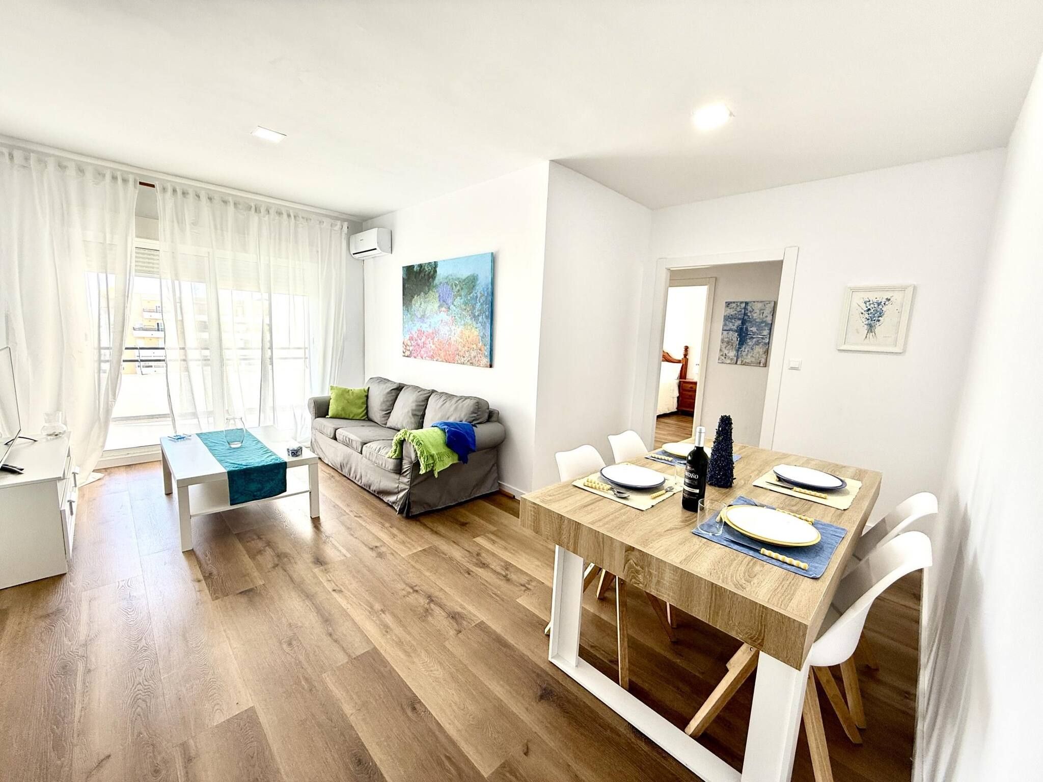 Un salon moderne comprenant un coin repas, un canapé gris agrémenté de coussins, une table à manger en bois pour quatre personnes et un tableau accroché au mur.
