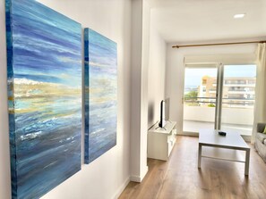 Un salon moderne doté d’une grande fenêtre, d’un téléviseur à écran plat et de deux tableaux abstraits accrochés au mur.