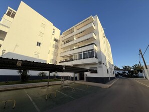 A multi-story building with a flat facade, balconies, and a covered parking area with a wheelchair ramp.