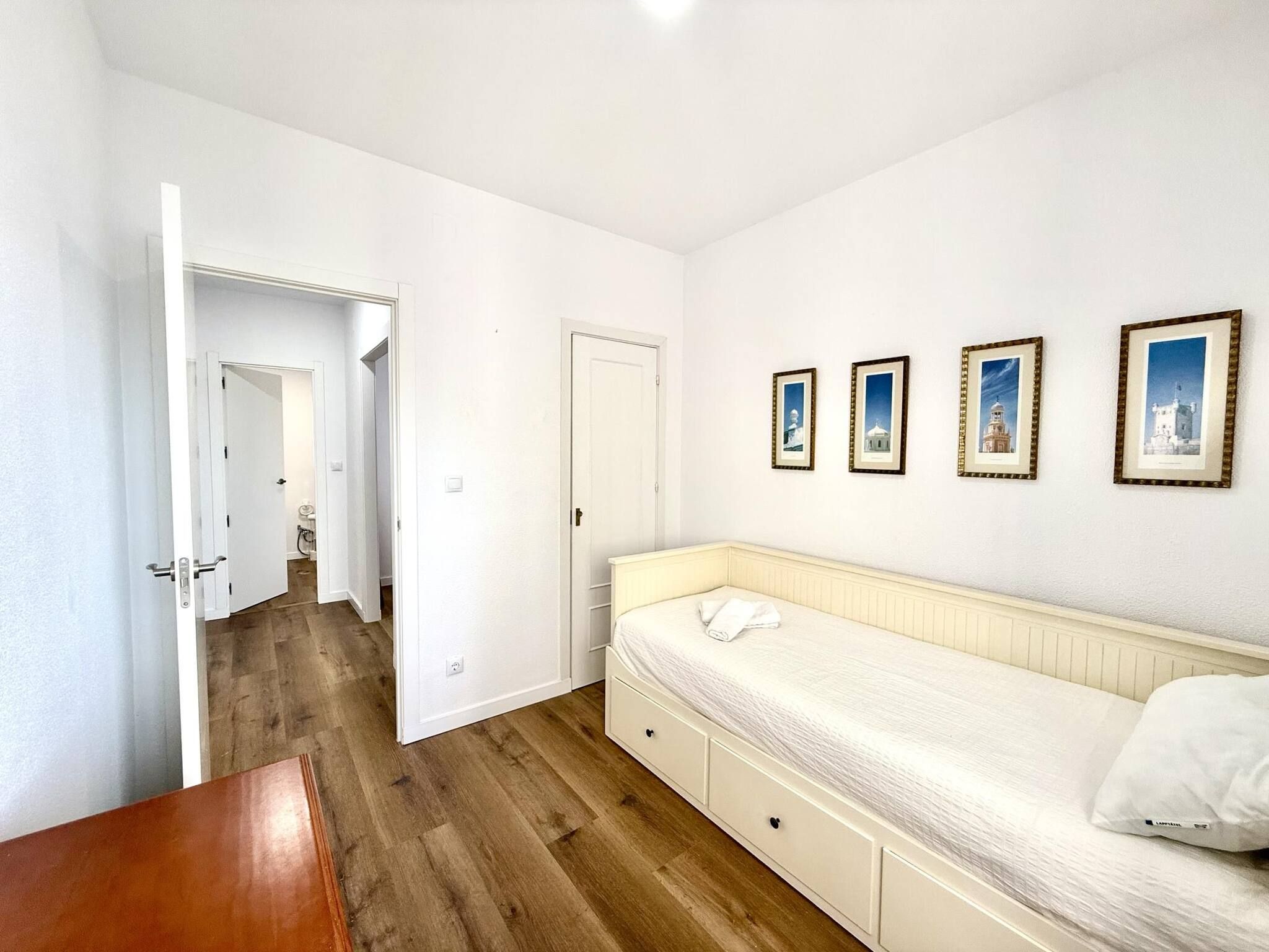 A bedroom with a bed, a wooden floor, a white door, and framed pictures on the wall.