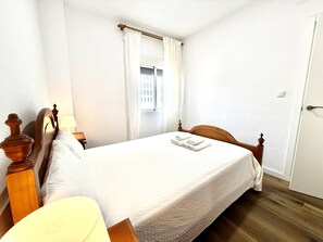 Une chambre d’hôtel avec un lit simple, une table de chevet avec une lampe, une fenêtre avec des rideaux et une porte.