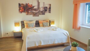 Une chambre à coucher avec un lit, des lampes de chevet, une plante en pot et des œuvres d’art accrochées au mur.