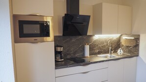 Une cuisine moderne équipée d’un four à micro-ondes encastré, d’une machine à café et d’un évier avec un plan de travail en marbre.