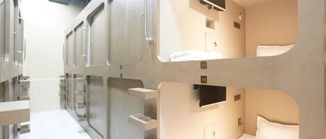 A modern hotel room with bunk beds, a television, and a small bathroom.